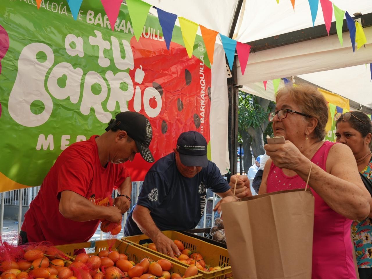 Señora sosteniendo bolsa de papel, al fondo dos vendedores clasificando las verduras