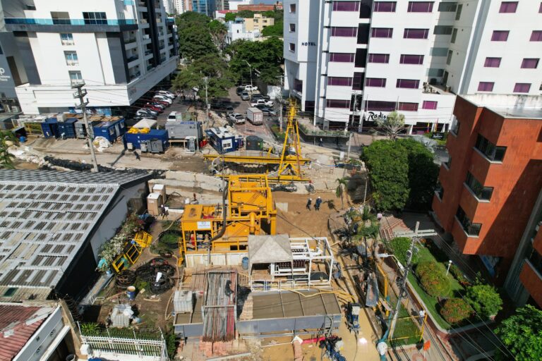 Plena ejecución, ubicada en una zona comercial, hay varias estructuras y equipo de color amarillo para excavación y perforación.