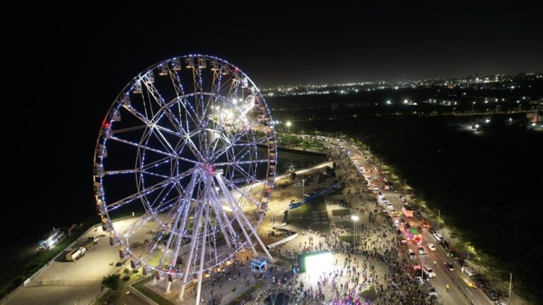 Vista aérea nocturna del Gran Malecón, iluminado por la gran noria con luces de colores y la presencia de cientos de personas que disfrutan del espacio a orillas del río Magdalena.