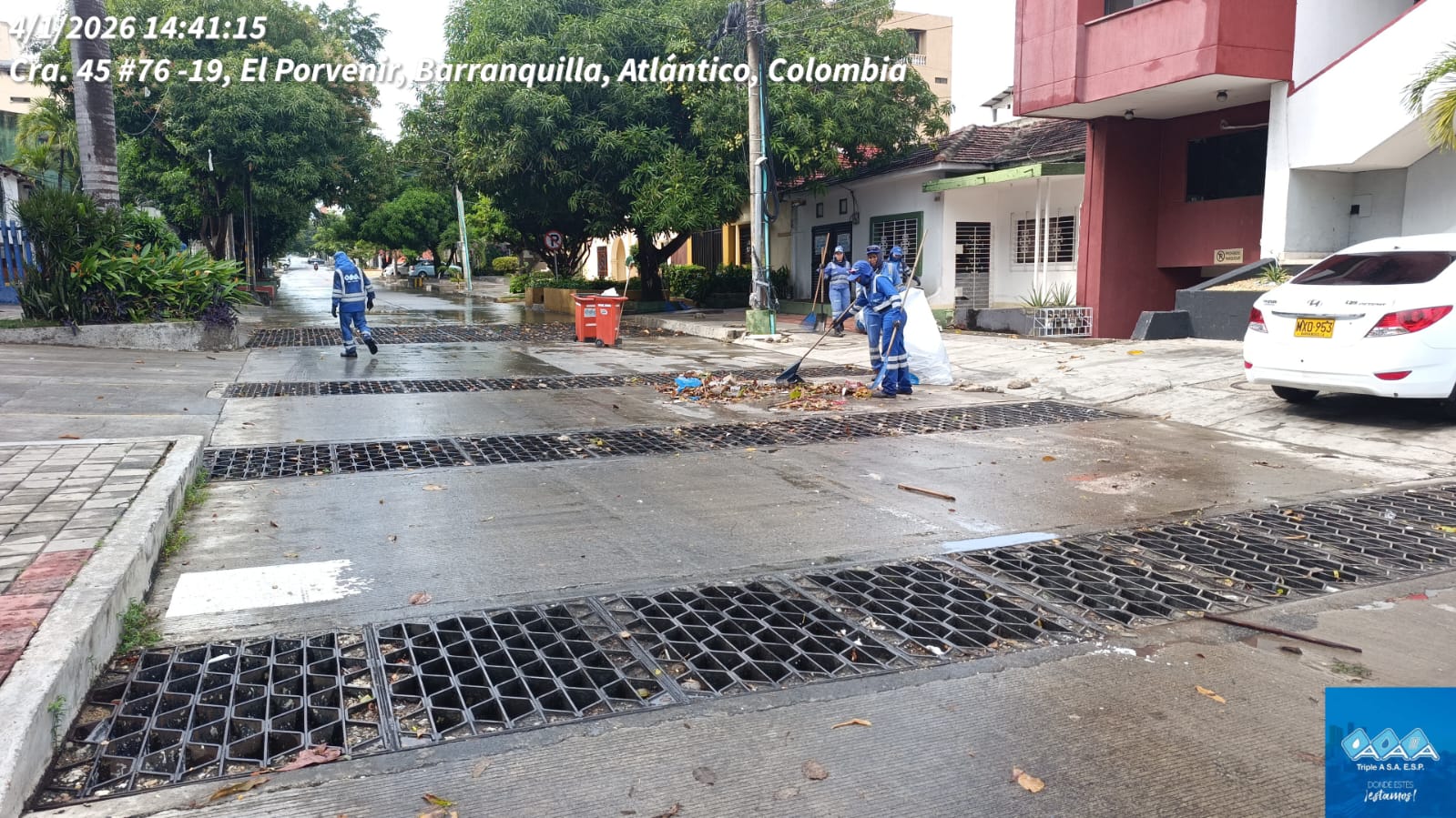 trabajadores de limpieza realizan labores de recolección de residuos. Llevan uniformes de protección azul y están retirando hojas, basura y sedimentos acumulados sobre la vía y alrededor de unas rejillas de drenaje pluvial ubicadas en el pavimento.