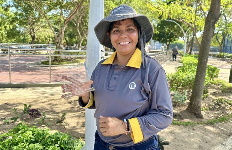 Selena, mujer con discapacidad auditiva portando un reconocimiento con su uniforme de Dolmen en su área de trabajo