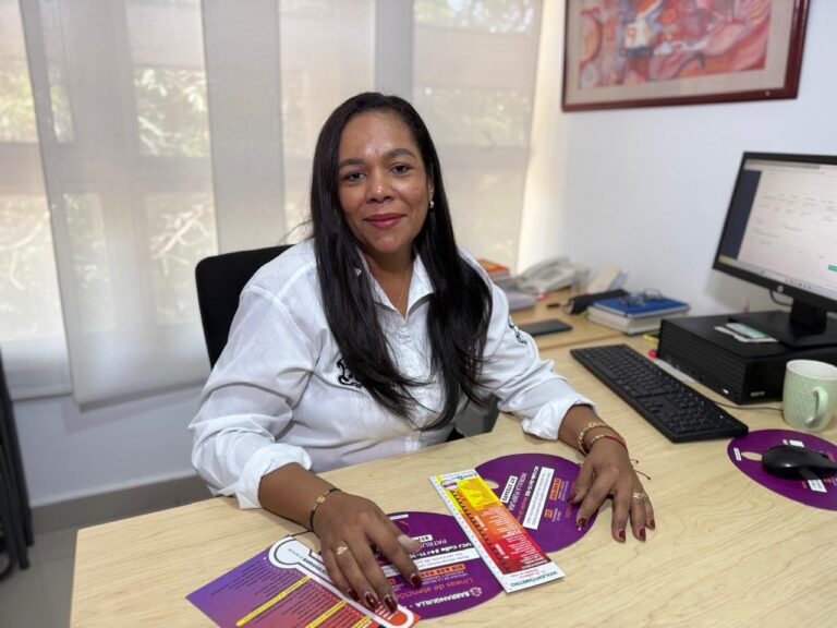 Funcioaria con camisa blanca institucional, sentada en escritorio.