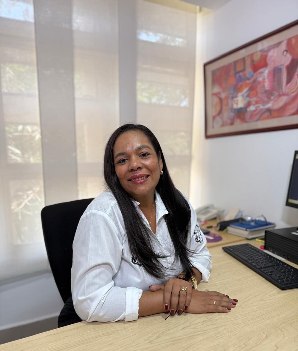 Imagen vertical de funcionaria en plano medio, sentada frente a escritorio.