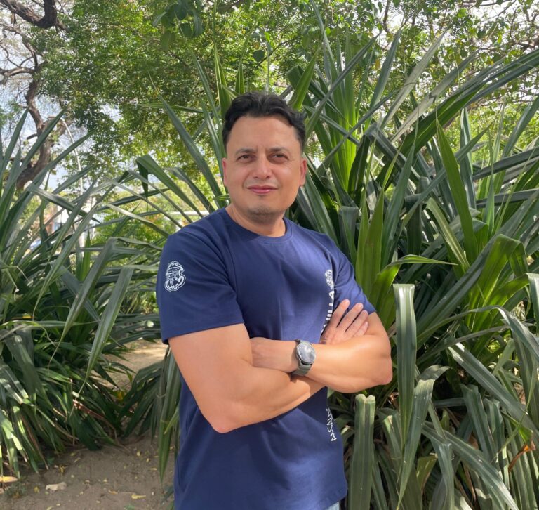 Funcionario en plano medio, con brazos cruzados y un fondo de un jardin.